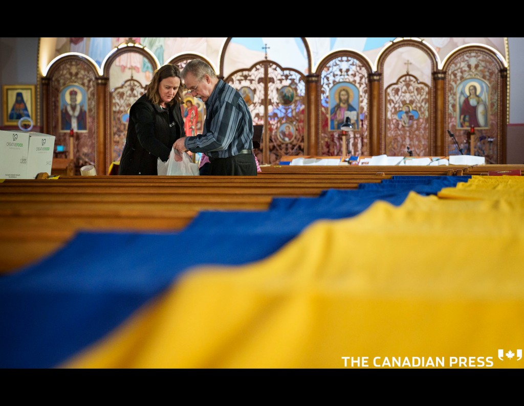A volunteer sorts through donations destined to Ukraine with a large Ukrainian flag draped over the pews at the St. Michael's Ukrainian Catholic Church in Montreal on Friday, March 25, 2022. Most goods are destined for overseas while others are needed for refugees arriving in Montreal. THE CANADIAN PRESS/Paul Chiasson